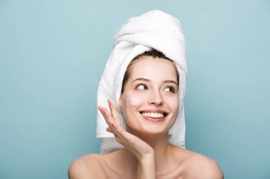 happy attractive girl applying moisturizing facial mask while looking away isolated on blue clipart