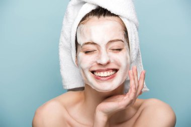 happy girl with moisturizing facial mask touching face with closed eyes isolated on blue clipart