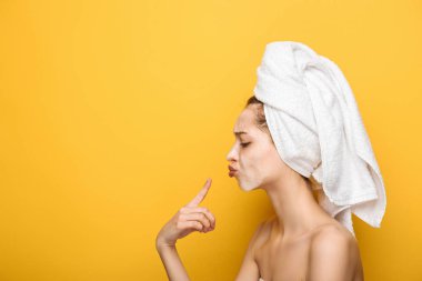 side view of girl with moisturizing facial mask pointing with finger at lips on yellow background clipart