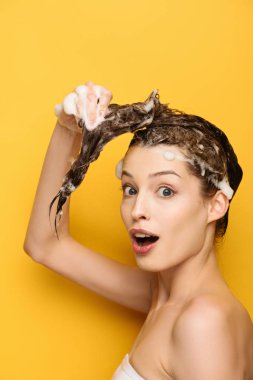 excited girl looking at camera while washing hair on yellow background clipart