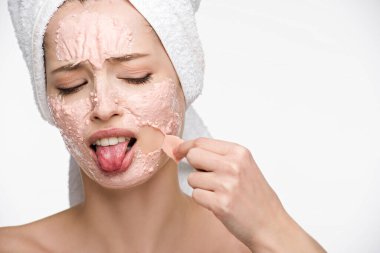 displeased girl removing peeling mask from face and sticking out tongue isolated on white clipart