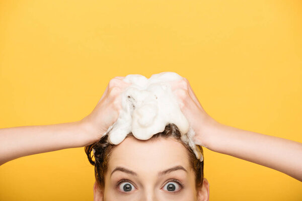 cropped view of excited girl with wide open eyes looking at camera while washing hair isolated on yellow
