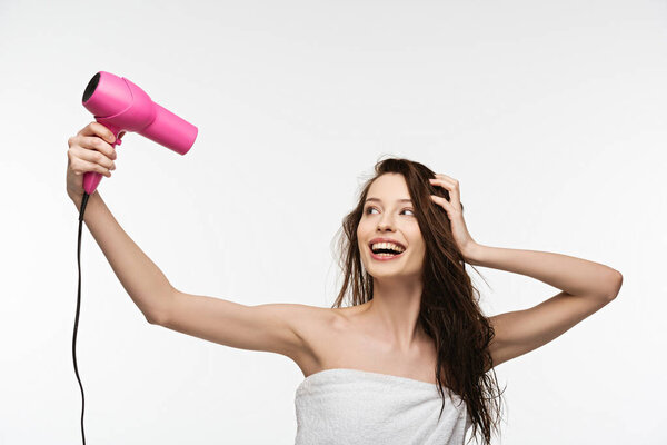 cheerful girl drying long hair with hair dryer isolated on white