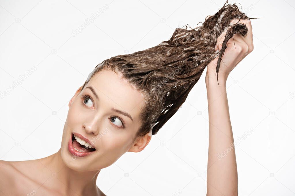 excited young woman with open mouth washing long hair isolated on white
