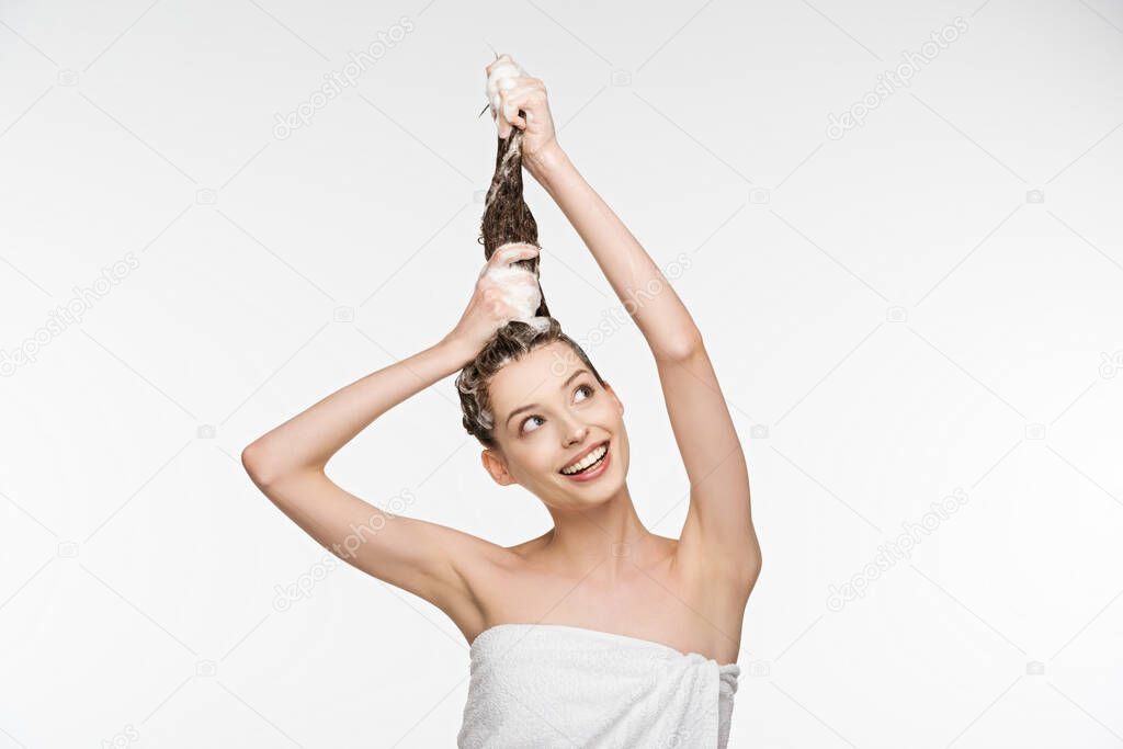 happy young woman washing long hair while looking away isolated on white