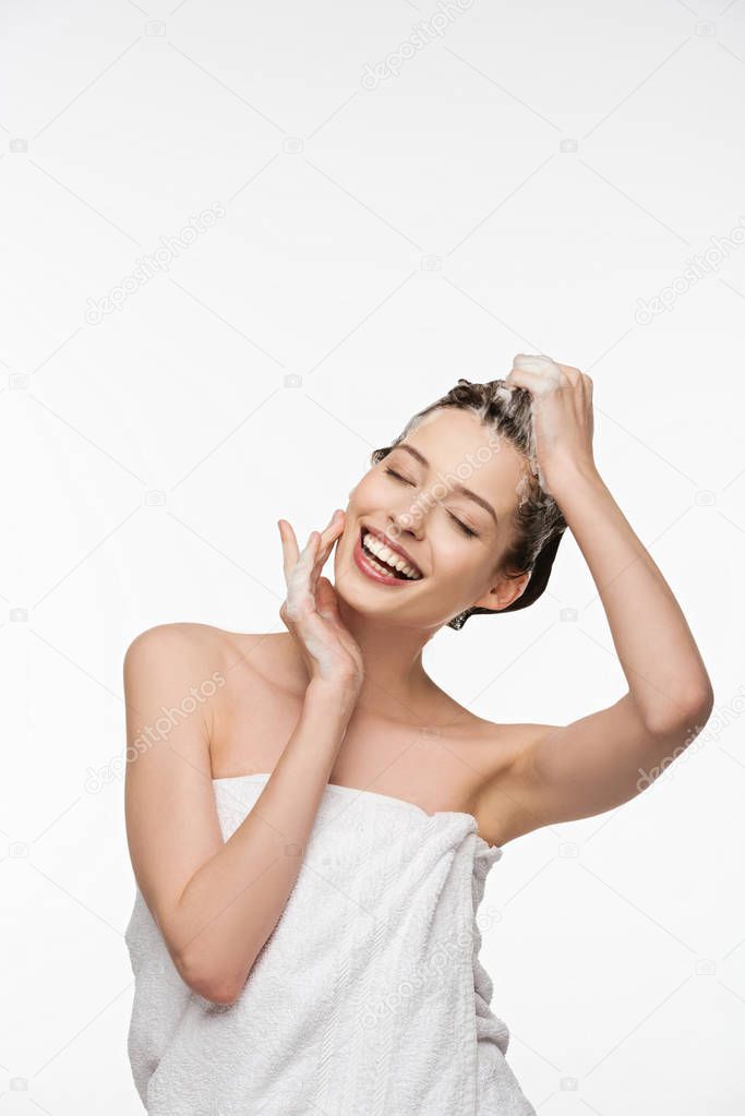 smiling girl washing hair with closed eyes while touching face isolated on white