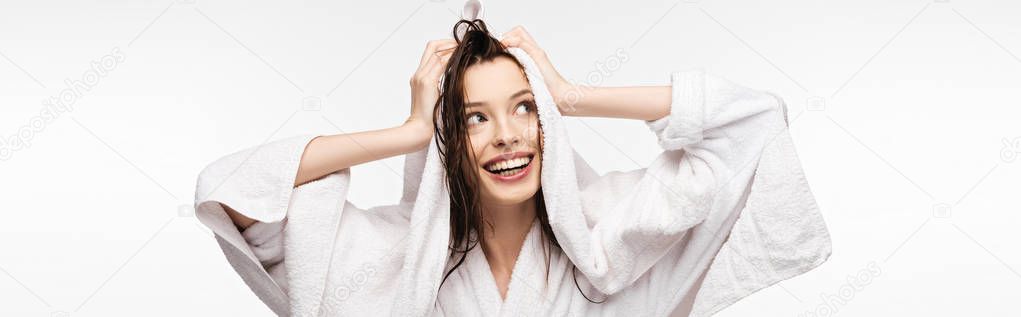 panoramic shot of happy girl wiping wet clean hair with white terry towel while looking away isolated on white
