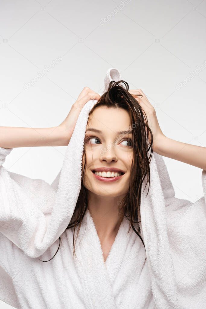 smiling girl wiping wet clean hair with white towel while looking away isolated on white