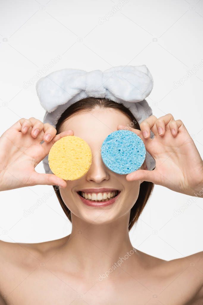smiling girl covering eyes with colorful cosmetic sponges isolated on white