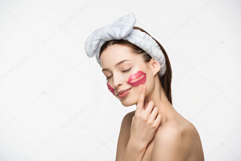 smiling girl with closed eyes pointing with finger at lip-shaped collagen patch on face isolated on white 