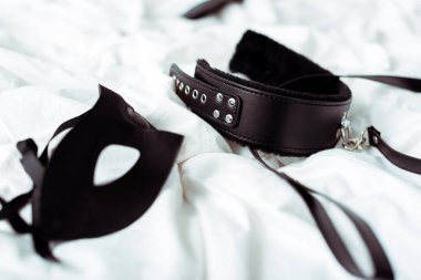 beyaz yatak üzerine bdsm tasma ve göz maskesi seçici odak 