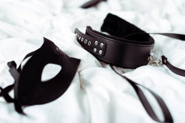 selective focus of bdsm leash and eye mask on white bedding  clipart