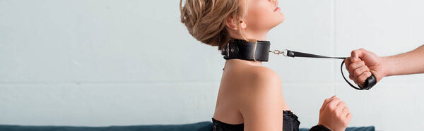 panoramic shot of man in holding bdsm leash on submissive woman