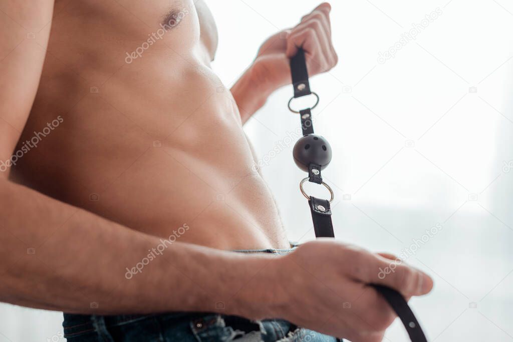 cropped view of shirtless man holding gag in bedroom 