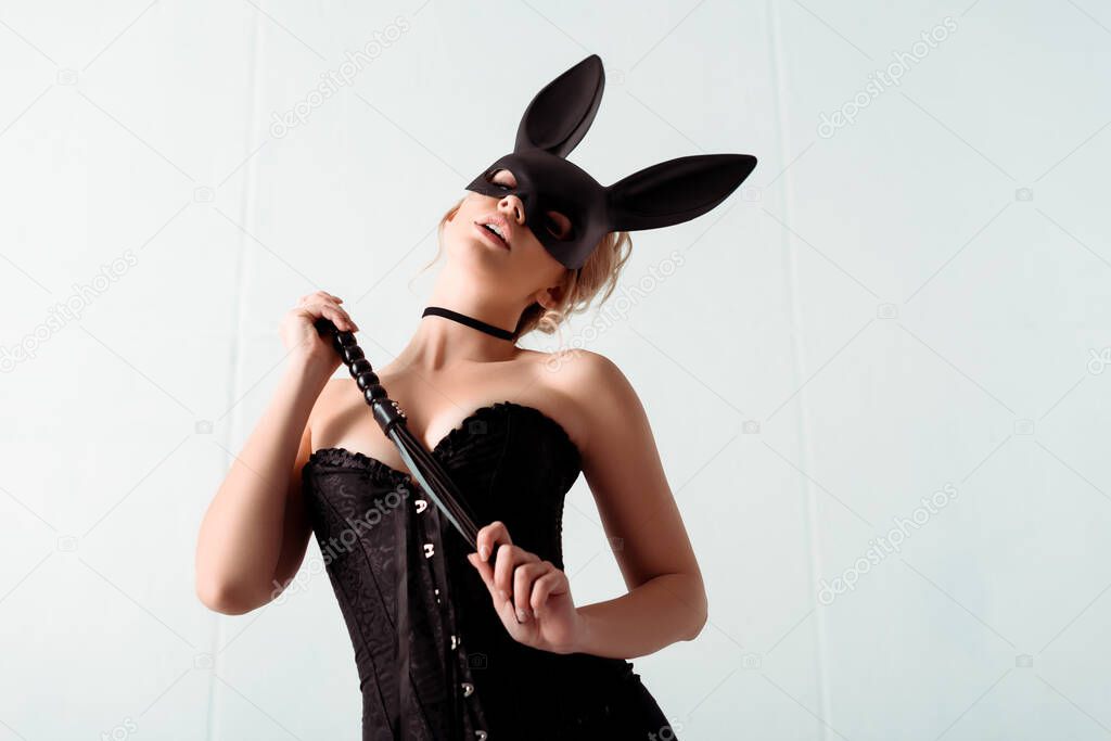 seductive young woman in bunny mask and corset holding flogging whip 