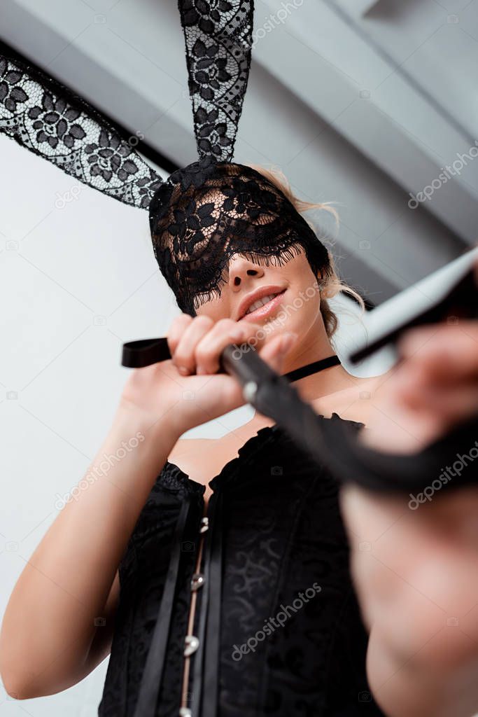 low angle view of blindfolded woman in rabbit mask holding flogging whip 