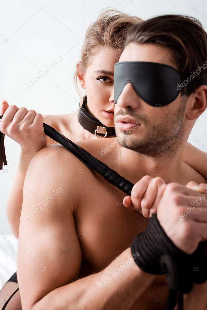 dominant girl holding flogging whip near blindfolded man 