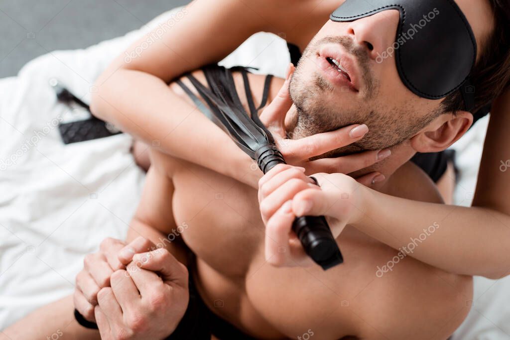 dominant woman holding flogging whip near blindfolded man 