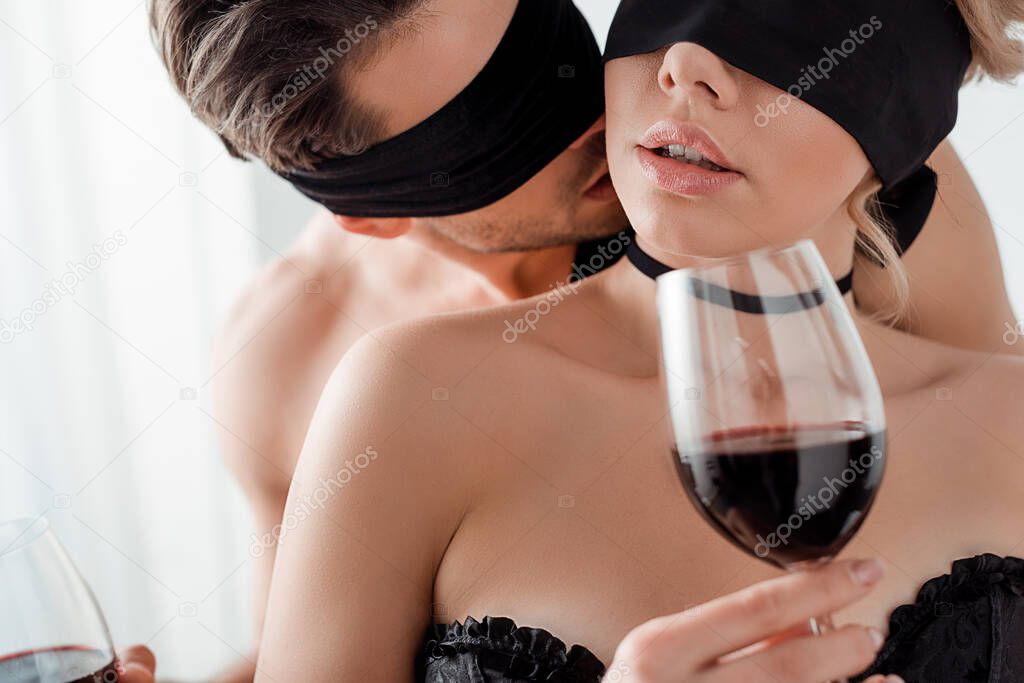 blindfolded man kissing woman with glass of wine 