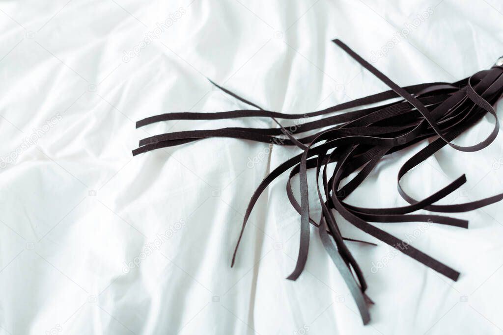 black leather flogging whip on white bedding 