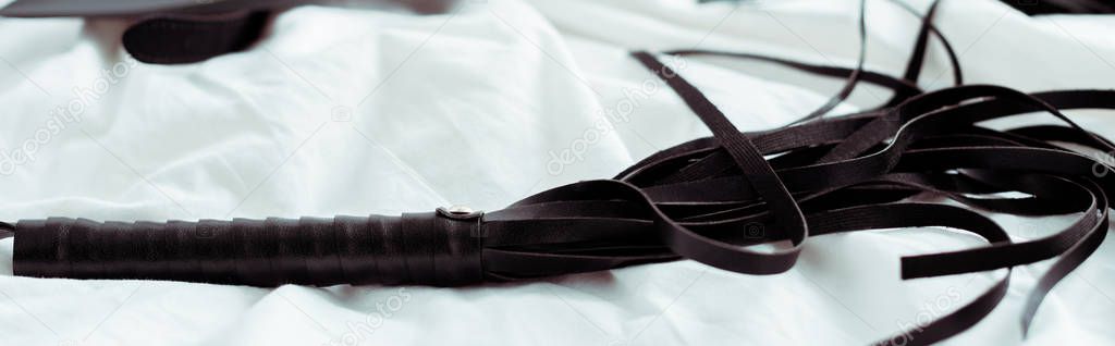 panoramic shot of leather flogging whip on white bedding 
