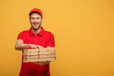 Kırmızı üniformalı mutlu teslimatçı sarı kutuya izole edilmiş pizza kutuları veriyor.