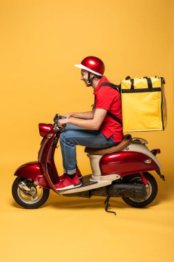 Sırt çantalı, motosikletli, sarı arka planlı teslimatçının yan görüntüsü