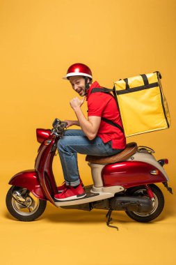 Sırt çantalı, motosikletli, sarı arka planlı mutlu teslimatçının yan görüntüsü
