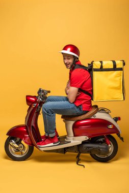 Sırt çantalı teslimatçının yan görünüşü ve sarı arka planda scooterlı çapraz kollar.