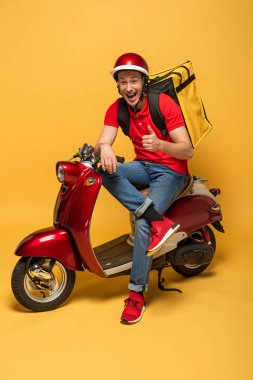 Motosikletli mutlu teslimatçı sarı arka planda baş parmağını gösteriyor.