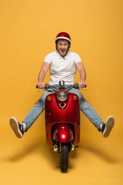 Sarı arka planda motosiklet süren kasklı mutlu teslimatçı.