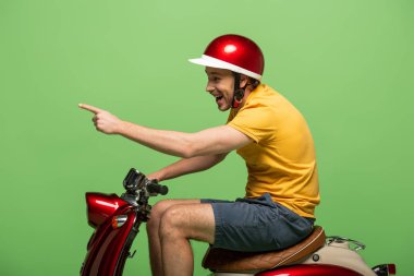 Sarı üniformalı mutlu teslimatçının yandan görünüşü, yeşilde izole edilmiş scooter 'ı işaret ediyor.