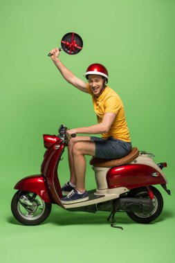 Sarı üniformalı mutlu teslimatçının yandan görünüşü. Elinde kızartma tavası, üstünde scooterlı yeşil.
