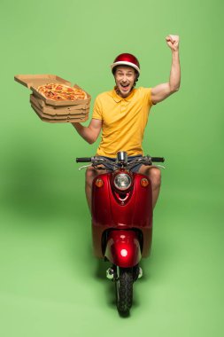 Sarı üniformalı mutlu teslimatçı scooter 'da pizza dağıtıyor ve yeşile evet işareti yapıyor.