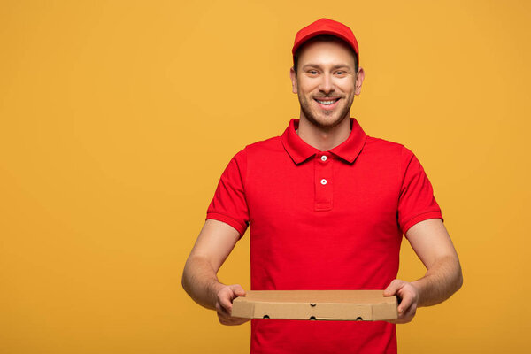 happy delivery man in red uniform holding pizza box isolated on yellow