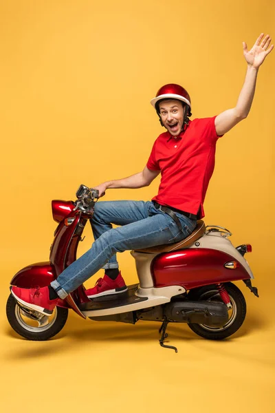 黄色い背景に手を振っているスクーターの配達人の側面図 — ストック写真