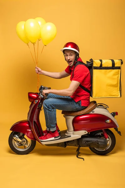 黄色の背景に風船とバックパック付きスクーターの興奮配達人の側面図 — ストック写真