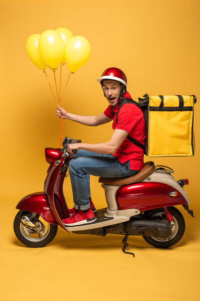 side view of excited delivery man with balloons and backpack on scooter on yellow background