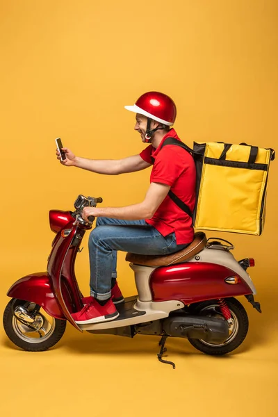 带背包的送货员的侧面视图 在黄色背景下的智能手机上自拍 — 图库照片