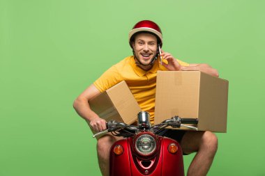 happy delivery man in yellow uniform on scooter with boxes talking on smartphone isolated on green clipart
