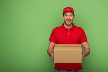 smiling delivery man in red uniform holding parcel on green
