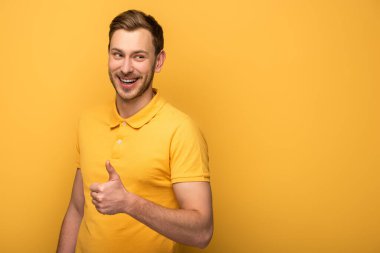 Sarı elbiseli mutlu yakışıklı adam sarı arka planda baş parmağını gösteriyor.