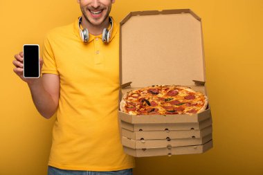 Sarı kulaklıklı, elinde pizza ve telefon olan mutlu bir adamın sarı arka planda görüntüsü.