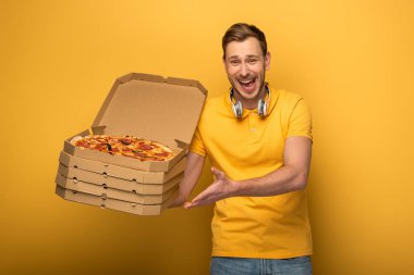 Sarı kulaklıklı mutlu adam sarı arka planda pizza tutuyor.