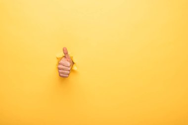 cropped view of man showing thumb up through yellow paper hole  clipart