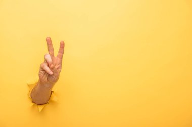 cropped view of man showing peace sign through yellow paper hole  clipart
