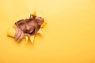 Heyecanlı yakışıklı adam sarı kağıt delikten bakıyor. 