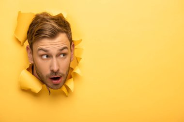 shocked handsome man with head in yellow paper hole  clipart