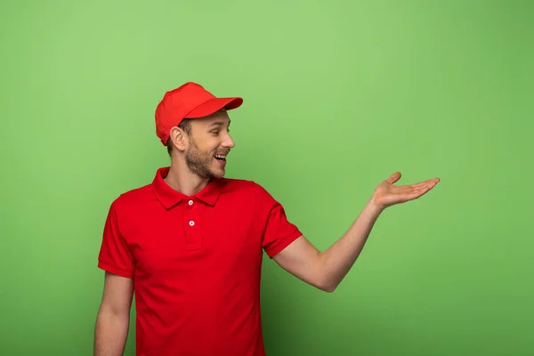 Happy Delivery Man Red Uniform Pointing Hand Aside Green — Stock Photo, Image