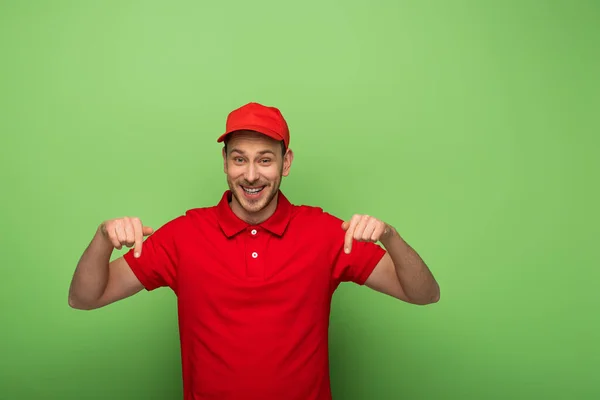 Leende Leverans Man Röd Uniform Pekar Med Fingret Ner Grön — Stockfoto